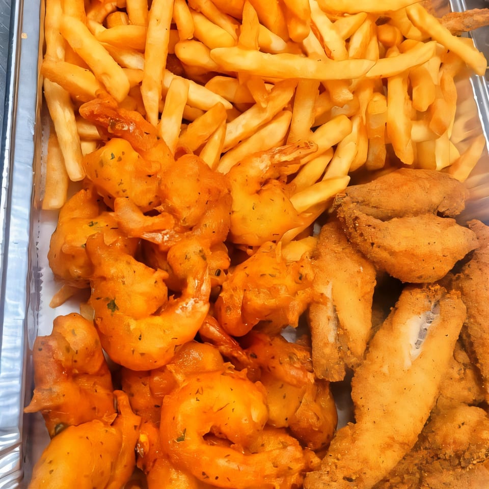 A takeout container filled with golden french fries, crispy fried shrimp, and breaded fish fillets.