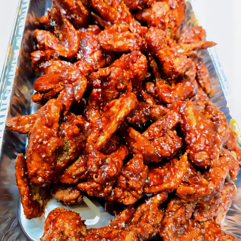 A large tray filled with numerous pieces of dark red, saucy chicken wings.