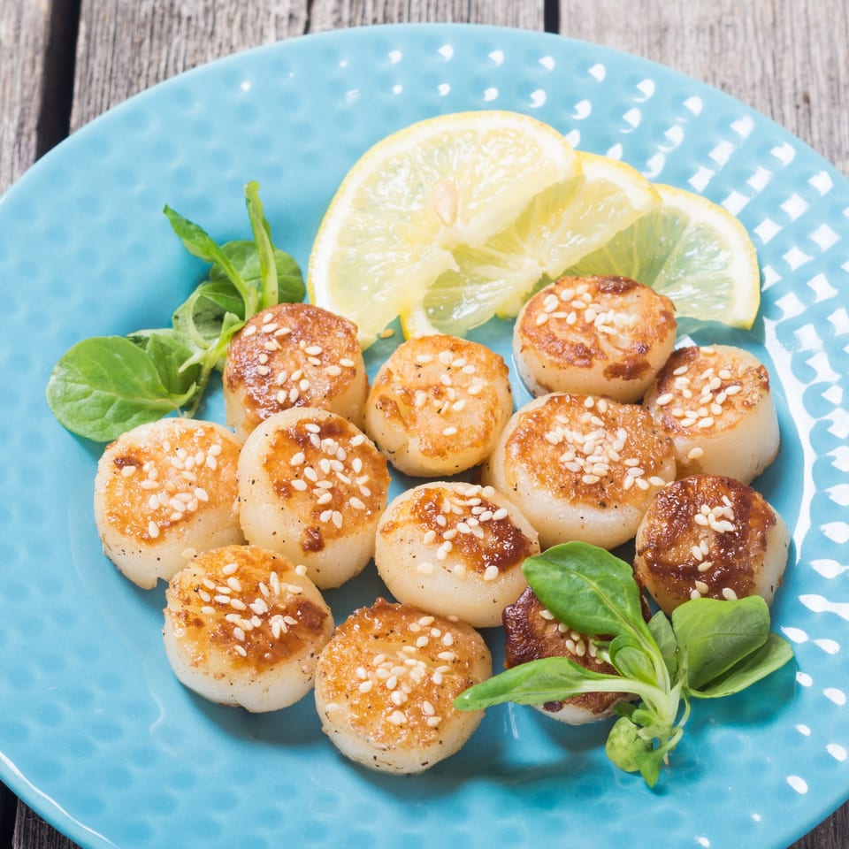 Walton's Fresh Fish Seafood: Pan-seared scallops with sesame seeds, lemon slices, and greens on a blue plate.