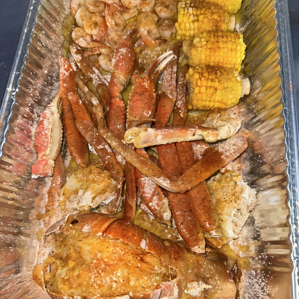A foil pan filled with seasoned shrimp, crab legs, and corn on the cob.
