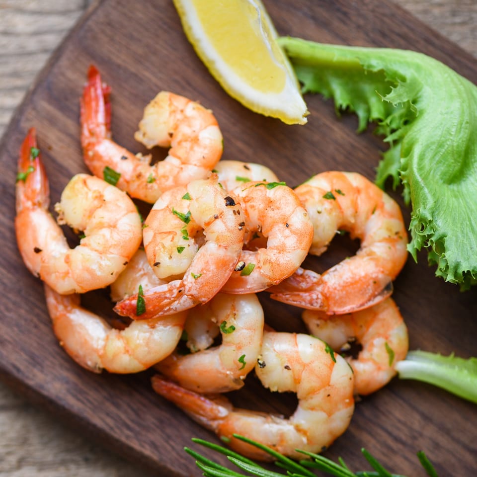 Grilled shrimp with parsley, lemon, and lettuce on a dark wooden board.